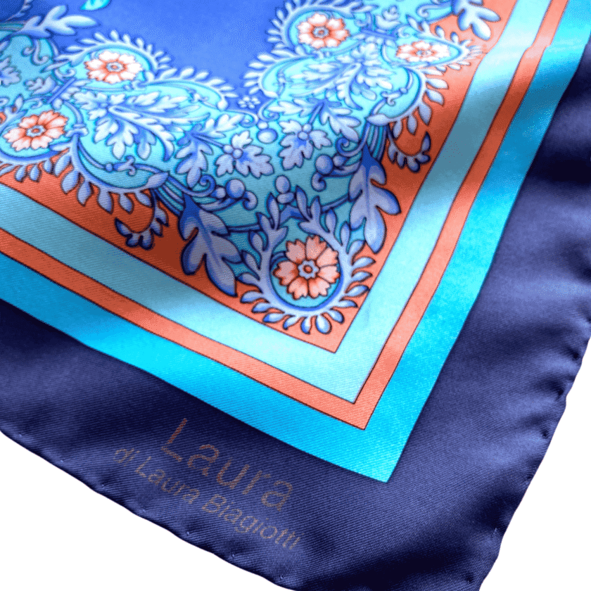 Détail coin Carré Dôme — signature Laura Biagiotti, bordure marine satinée, arabesques turquoise et orange, grand foulard soie vintage