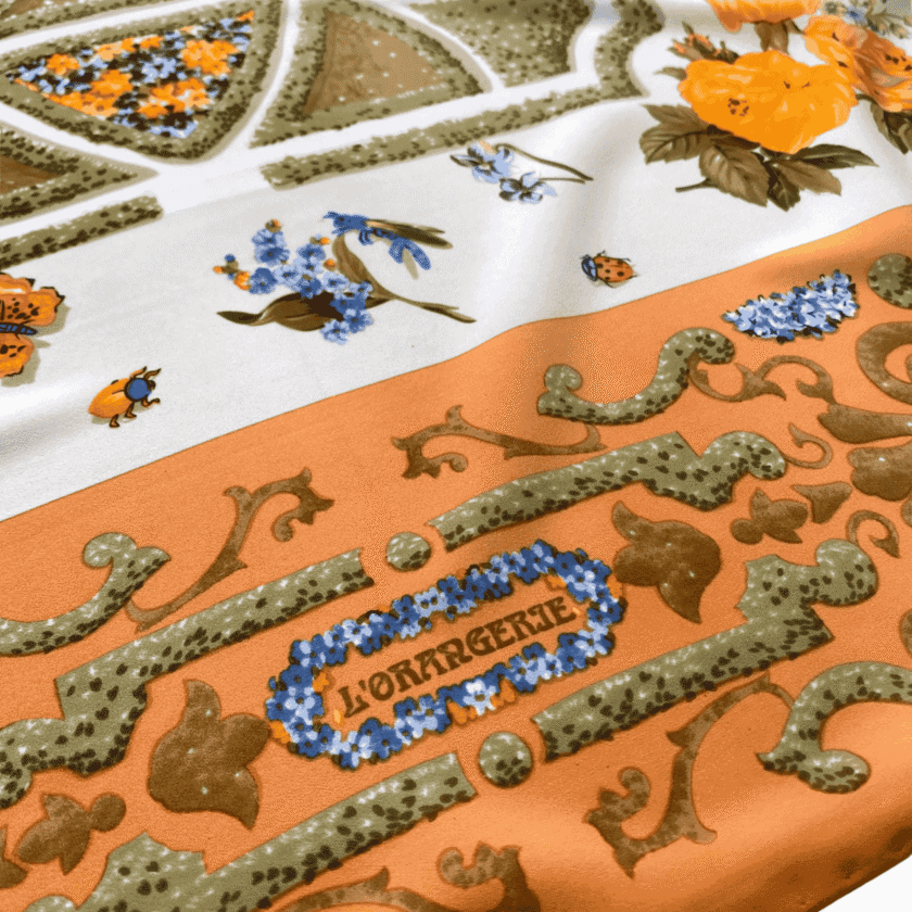 Foulard en soie imprimé femme vintage – détail signature L'Orangerie sur bordure abricot, tombé satiné, motifs floraux et arabesques vert olive